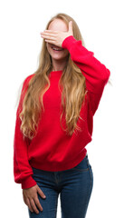 Wall Mural - Blonde teenager woman wearing red sweater smiling and laughing with hand on face covering eyes for surprise. Blind concept.