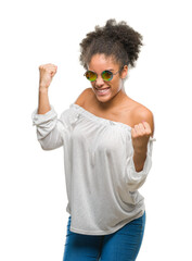 Canvas Print - Young afro american woman wearing sunglasses over isolated background very happy and excited doing winner gesture with arms raised, smiling and screaming for success. Celebration concept.