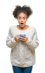 Canvas Print - Young afro american woman driking cup of coffee over isolated background scared in shock with a surprise face, afraid and excited with fear expression