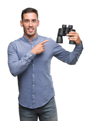 Canvas Print - Handsome young man looking through binoculars very happy pointing with hand and finger