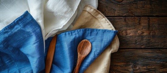 Canvas Print - Kitchen towels in blue and off-white, accompanied by a wooden spoon and knife, set against a dark wood backdrop, featuring a central copy space image.