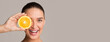 © Prostock-studio - Pretty young woman holding orange half over her eye and smiling, colorful studio background, panorama with copy space