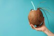 © Sweettymojidesign - A hand gripping a fresh coconut with a straw against a solid blue backdrop with space for text