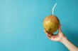 © Sweettymojidesign - A hand gripping a fresh coconut with a straw against a solid blue backdrop with space for text