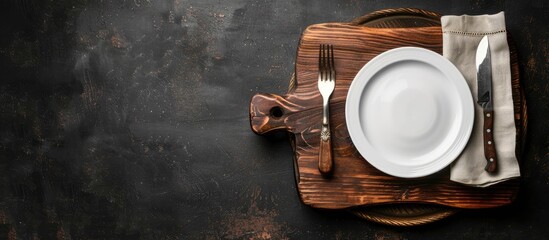 Aufkleber - Top view of an old wooden board with a white plate, fork, and knife on a dark background providing copy space image.