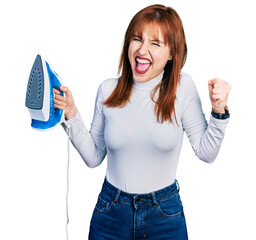 Poster - Redhead young woman holding electric steam iron screaming proud, celebrating victory and success very excited with raised arms