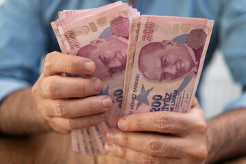 Male tourist holds Turkish lira banknotes in hands counting money after currency exchange procedure with favorable rates sitting at desk in local bank