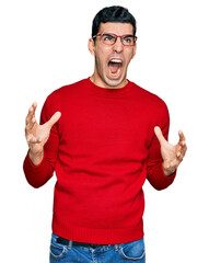 Wall Mural - Handsome hispanic man wearing casual clothes and glasses crazy and mad shouting and yelling with aggressive expression and arms raised. frustration concept.