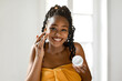 © Prostock-studio - African American woman with braided hair smiles as she applies moisturizer to her face in a bathroom. She is wearing a yellow towel and is holding a container of moisturizer in her other hand.