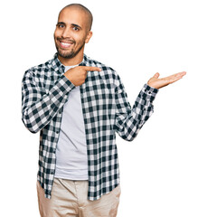 Poster - Hispanic adult man wearing casual clothes amazed and smiling to the camera while presenting with hand and pointing with finger.