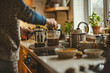 © BetterPhoto - A person making coffee with French presses on a kitchen counter, surrounded by various kitchen items, representing a cozy morning routine at home.