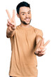 © Krakenimages.com - Hispanic man with beard wearing casual t shirt smiling with tongue out showing fingers of both hands doing victory sign. number two.