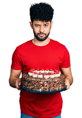 Canvas Print - Young arab man with beard celebrating birthday holding big chocolate cake skeptic and nervous, frowning upset because of problem. negative person.