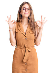 Wall Mural - Young beautiful blonde woman wearing casual clothes and glasses relaxed and smiling with eyes closed doing meditation gesture with fingers. yoga concept.