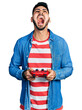 © Krakenimages.com - Young hispanic man with beard playing video game holding controller angry and mad screaming frustrated and furious, shouting with anger looking up.