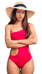 Young beautiful latin girl wearing swimwear and summer hat skeptic and nervous, disapproving expression on face with crossed arms. negative person.