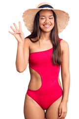 Sticker - Young beautiful latin girl wearing swimwear and summer hat showing and pointing up with fingers number four while smiling confident and happy.