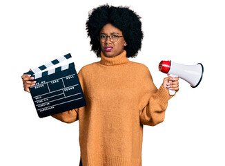 Canvas Print - Young african american woman holding video film clapboard and megaphone clueless and confused expression. doubt concept.