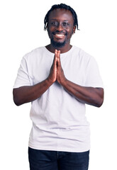 Poster - Young african american man with braids wearing casual white tshirt praying with hands together asking for forgiveness smiling confident.