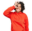 © Krakenimages.com - Young hispanic woman with curly hair wearing casual sweatshirt smiling happy doing ok sign with hand on eye looking through fingers