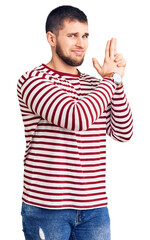 Sticker - Young handsome man wearing striped sweater holding symbolic gun with hand gesture, playing killing shooting weapons, angry face