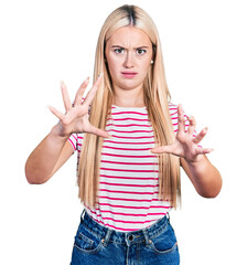 Wall Mural - Beautiful blonde woman wearing casual striped t shirt afraid and terrified with fear expression stop gesture with hands, shouting in shock. panic concept.