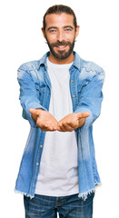 Wall Mural - Attractive man with long hair and beard wearing casual denim jacket smiling with hands palms together receiving or giving gesture. hold and protection