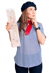 Wall Mural - Young beautiful blonde woman wearing french beret holding city map serious face thinking about question with hand on chin, thoughtful about confusing idea