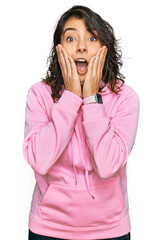 Canvas Print - Young hispanic woman wearing casual sweatshirt afraid and shocked, surprise and amazed expression with hands on face