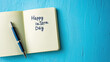 © Tati - Notebook with 'Happy Intern Day' written on page beside pen blue surface