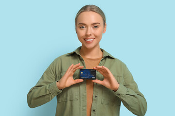 Wall Mural - Pretty young woman with credit card on blue background