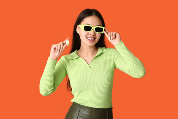 Canvas Print - Beautiful young Asian woman with chewing gum on orange background