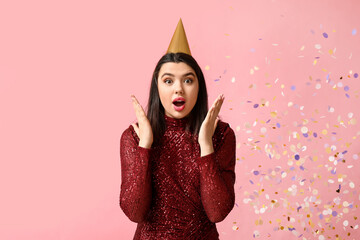 Poster - Shocked young woman in party hat and confetti on pink background