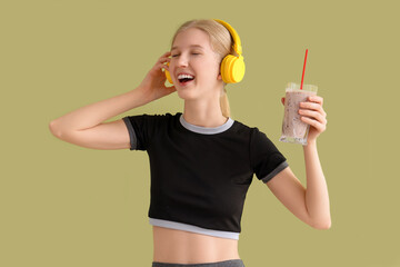 Sticker - Happy sporty young woman in headphones with healthy smoothie on green background