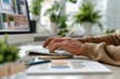 © porpia - Close-up of a person typing on a keyboard in a home office setting, surrounded by charts and greenery, representing productivity and remote work.