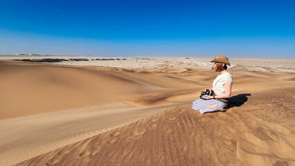 Lone women traveling in a desert with sand dunes and a clear blue sky in Namibia, Africa