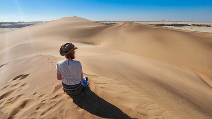 Lone women traveling in a desert with sand dunes and a clear blue sky in Namibia, Africa