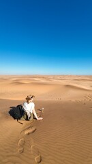 Sticker - Lone traveler sitting on the sand dunes under a clear blue sky in Namibia, Africa.