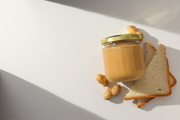 Wall Mural - Peanut paste in a glass jar with toast, on a light background.