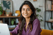 © btiger - Cheerful Indian Woman in Purple Shirt at Desk with Laptop in Cozy Home Office Smiling at Camera