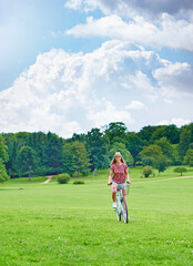 Canvas Print - Cycling, woman and happy in countryside for eco friendly or sustainable transportation in park. Blue sky, female person and travel or freedom in nature for journey, adventure and smile for sunshine