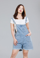 Portrait of Asian cute cheerful young girl wearing denim overalls, stylish model woman with happy and cool sweet smile standing posing isolated on white background, Teenage and youth fashion.