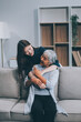 © ARMMY PICCA - Adult daughter old mom hugging sit on couch enjoy pleasant positive talk, remembering funny occasion from life spend weekend together, caring about older generation relatives express attention concept