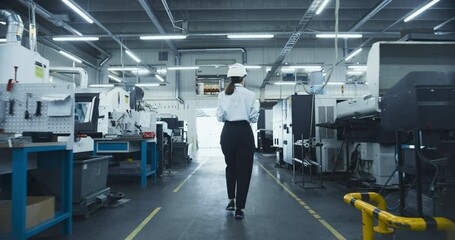 Leinwandbilder - Female Worker in a White Hard Hat Walks Through a Manufacturing Facility, Inspecting Machinery and Ensuring Operational Efficiency. Factory is Equipped with Advanced Automated Engineering Tools