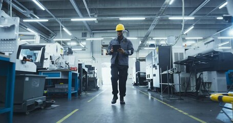 Aufkleber - African American Male Worker in a Yellow Hard Hat Walks Through a Modern Factory, Inspecting Equipment and Recording Data on a Tablet Computer. Facility is Equipped with Advanced Machinery