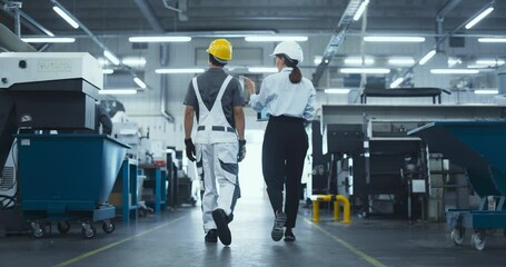 Leinwandbilder - Diverse Female and Male Technicians Walking Through a Modern Factory, Discussing Work. Young Man Wearing a Yellow Hard Hat and Overalls, Manager Dressed in Business Attire. Footage From the Back