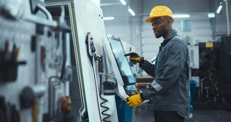 Leinwandbilder - African Male Engineer in a Yellow Hard Hat Operating a CNC Milling Machine in a Modern Factory. Young Technician Inserting Parameters on a Touch Screen Display, Automating Production Line