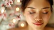 © Koborixgen - A serene woman with peaceful expression enjoying a relaxing spa treatment surrounded by beautiful pink flowers and soft ambient lighting.