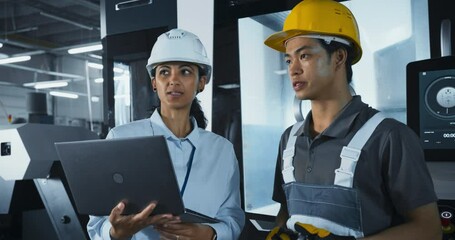 Leinwandbilder - Two Male and a Female Factory Employees Standing in a High Tech Manufacturing Facility, Discussing Operations and Production Machinery. Diverse Employees Wear Safety Gear and Use a Laptop Computer