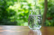 © p-fotography - pouring drinking water in to clear glass on wooden table in garden background.
